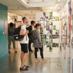 Visitors to the Norwich University of the Arts Degree Shows look at graphic design work next to a green wall