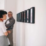 A visitor to the Norwich University of the Arts undergraduate degree show stands looking at multiple frames on a wall.