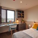 Bedroom at Duke Street Riverside showing a living area; bed, cushions, duvet, throw, green chair by a desk