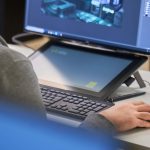 Creative technology student at NUA holds a mouse next to a keyboard, tablet and a screen