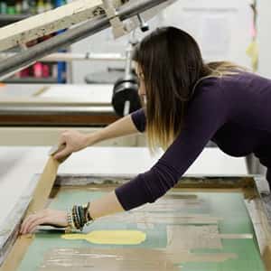 A student masks off the edge of a silkscreen to start printing on to fabric