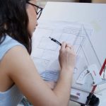 A student studying interior design at Norwich University of the Arts works calmly on a floorplan, using one of the drawing tables in the architecture and interior design studio space.