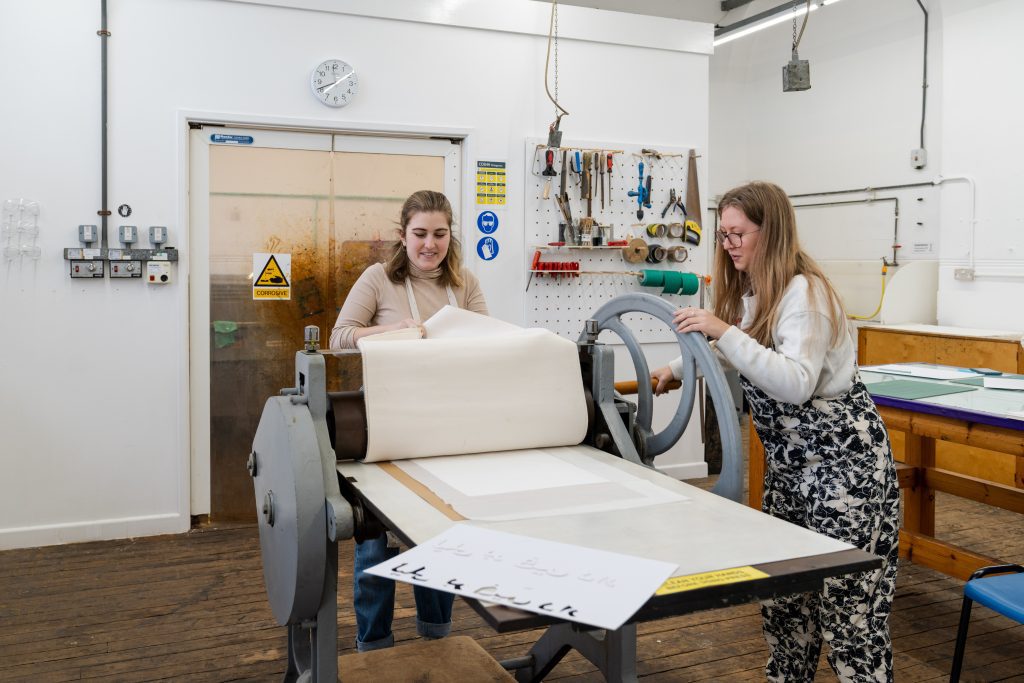 A photo of a technician helping a student use a large metal roller to emboss onto paper.