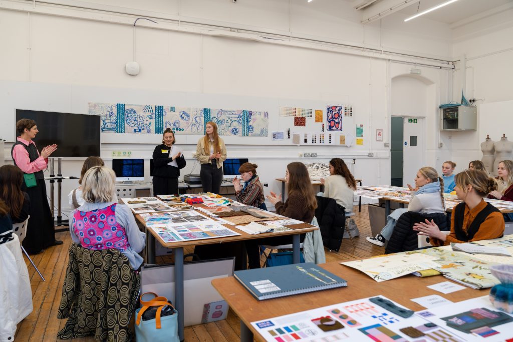 A photo of Textile Design students sat around tables listening to a talk by Kate Farley.