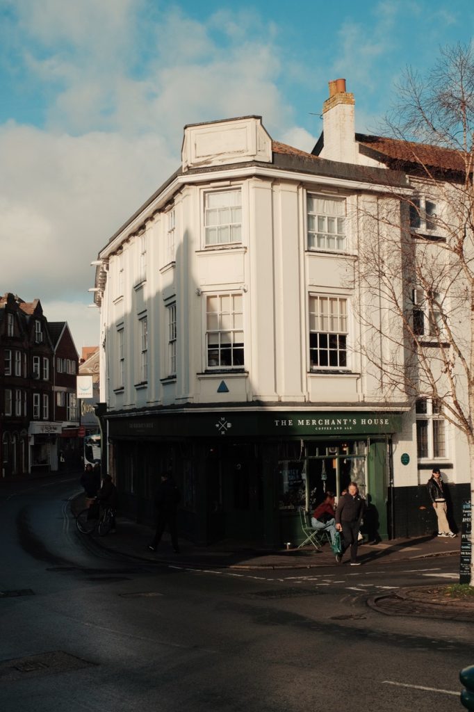 A photo of the Merchants coffee house in Norwich. A white building with greens doors and windows. 