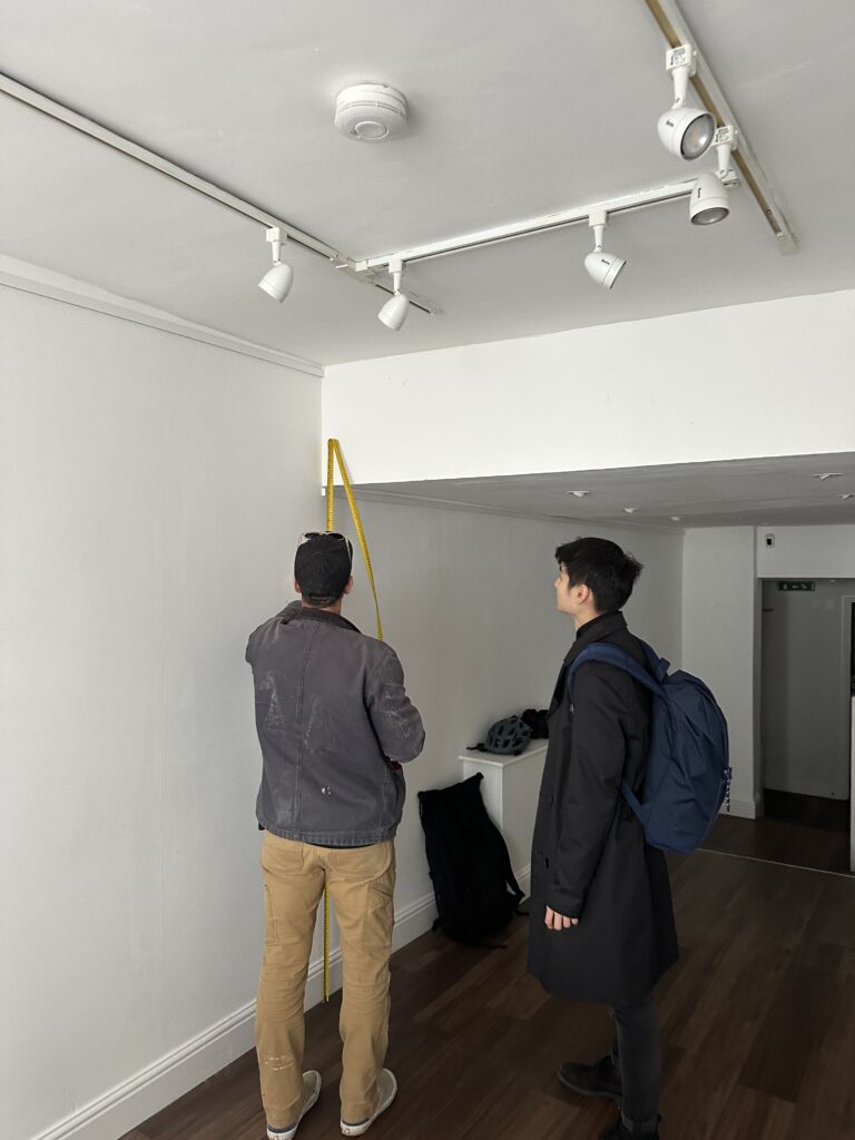 A photograph of Desmond Lau and someone else measuring a space. 