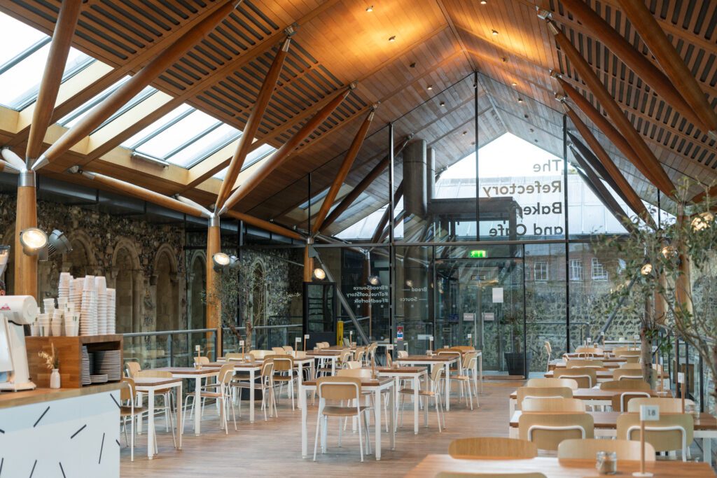 A photo of the cafe in Norwich Cathedral. The image is a wide shot of the room from floor to ceiling, filled with tables and chairs.