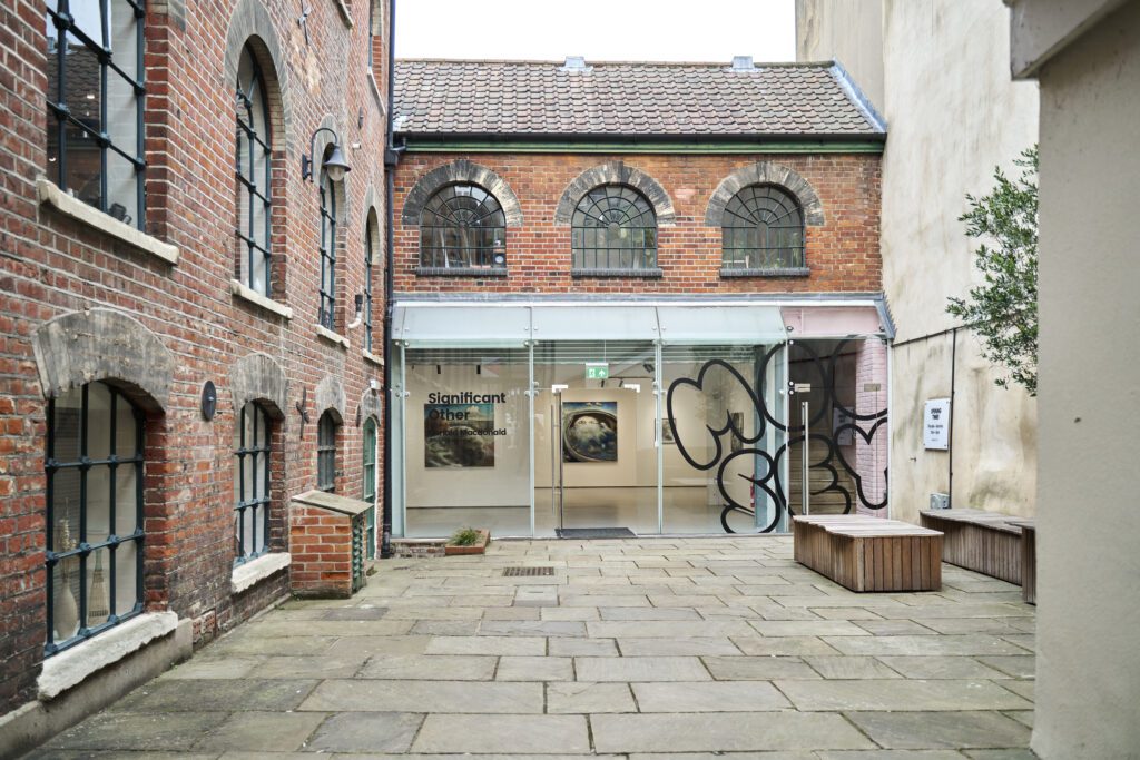 A photo of Moose Art Gallery in Norwich. The image is of the front of the red brick building with a glass front entrance. 