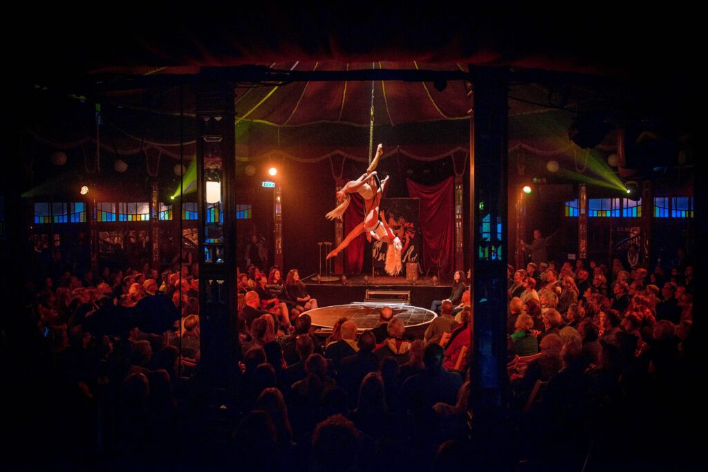 The photo is from The Norfolk & Norwich Festival. The image is of what looks like a circus/acrobatic performance with a large audience of people watching.  
